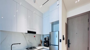 A modern kitchen with white cabinets, a stainless steel refrigerator, a gas stove, and a wooden door. - Premium Belvilla 1Bedroom in JVC with Pool & Gym (Dubai)