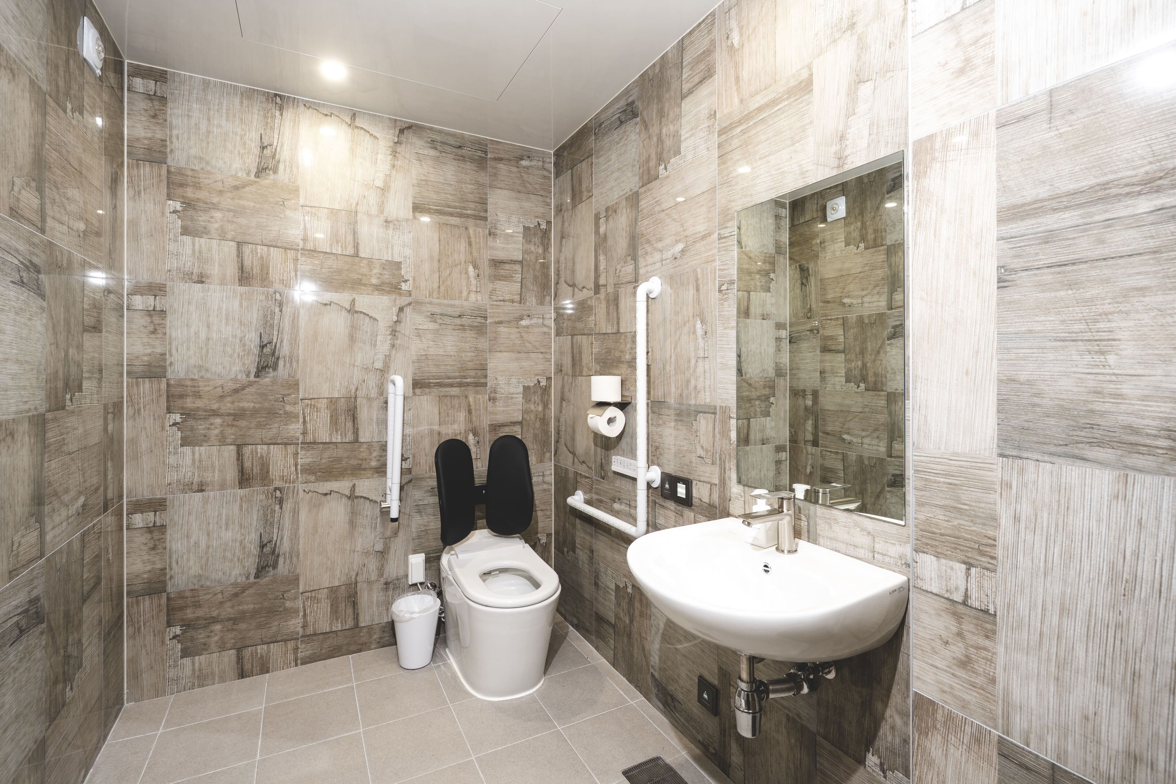 A modern bathroom with a toilet, bidet, and sink, all with marble-like wall tiles.