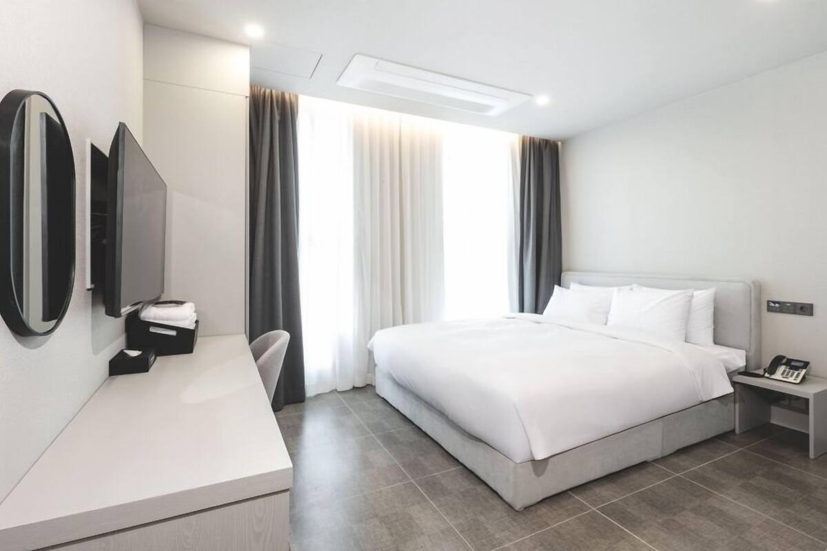 Quarto de hotel moderno com uma cama grande, uma escrivaninha com cadeira, televisão de tela plana e telefone ao lado da cama.