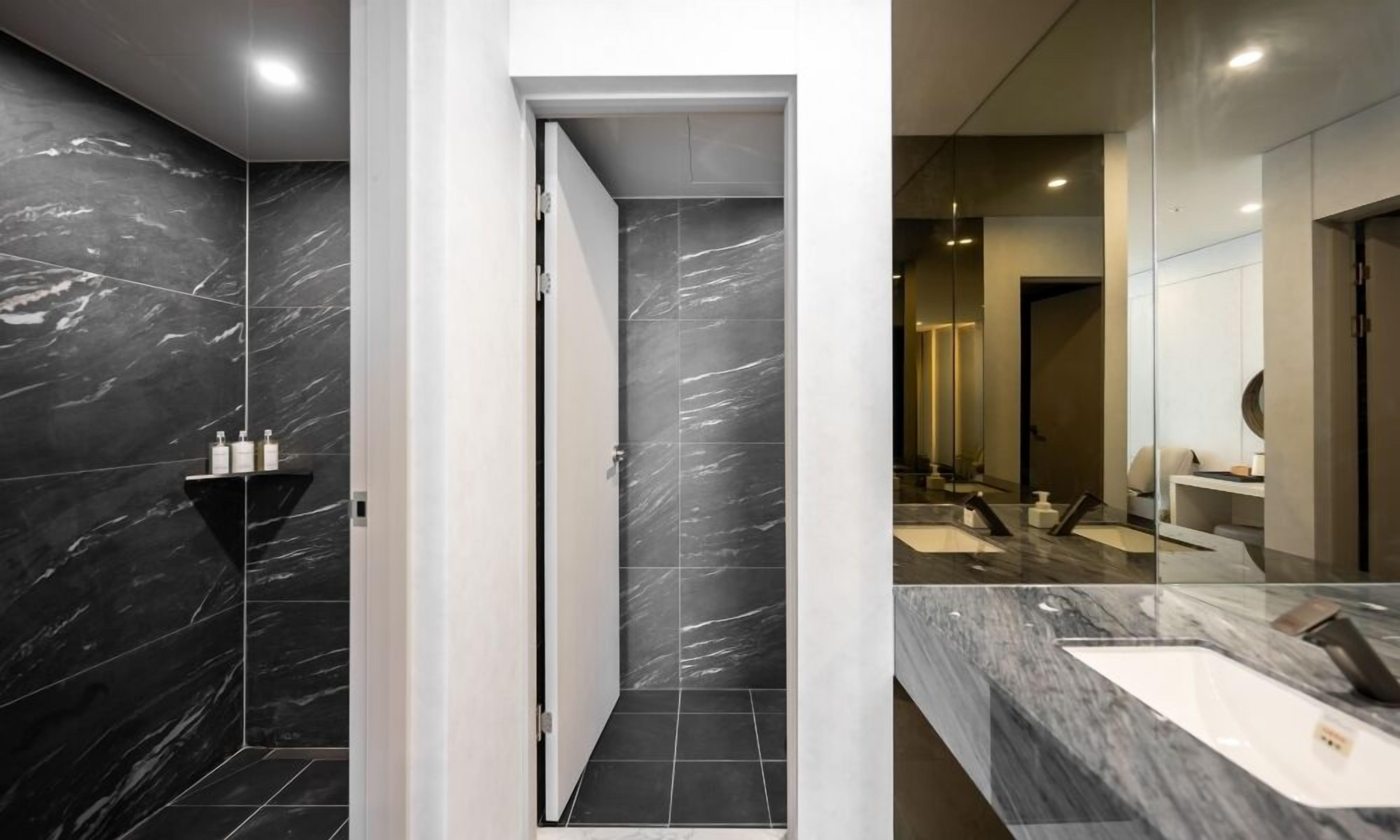 A modern bathroom with dark marble walls, a white door, and a large mirror above a sink.