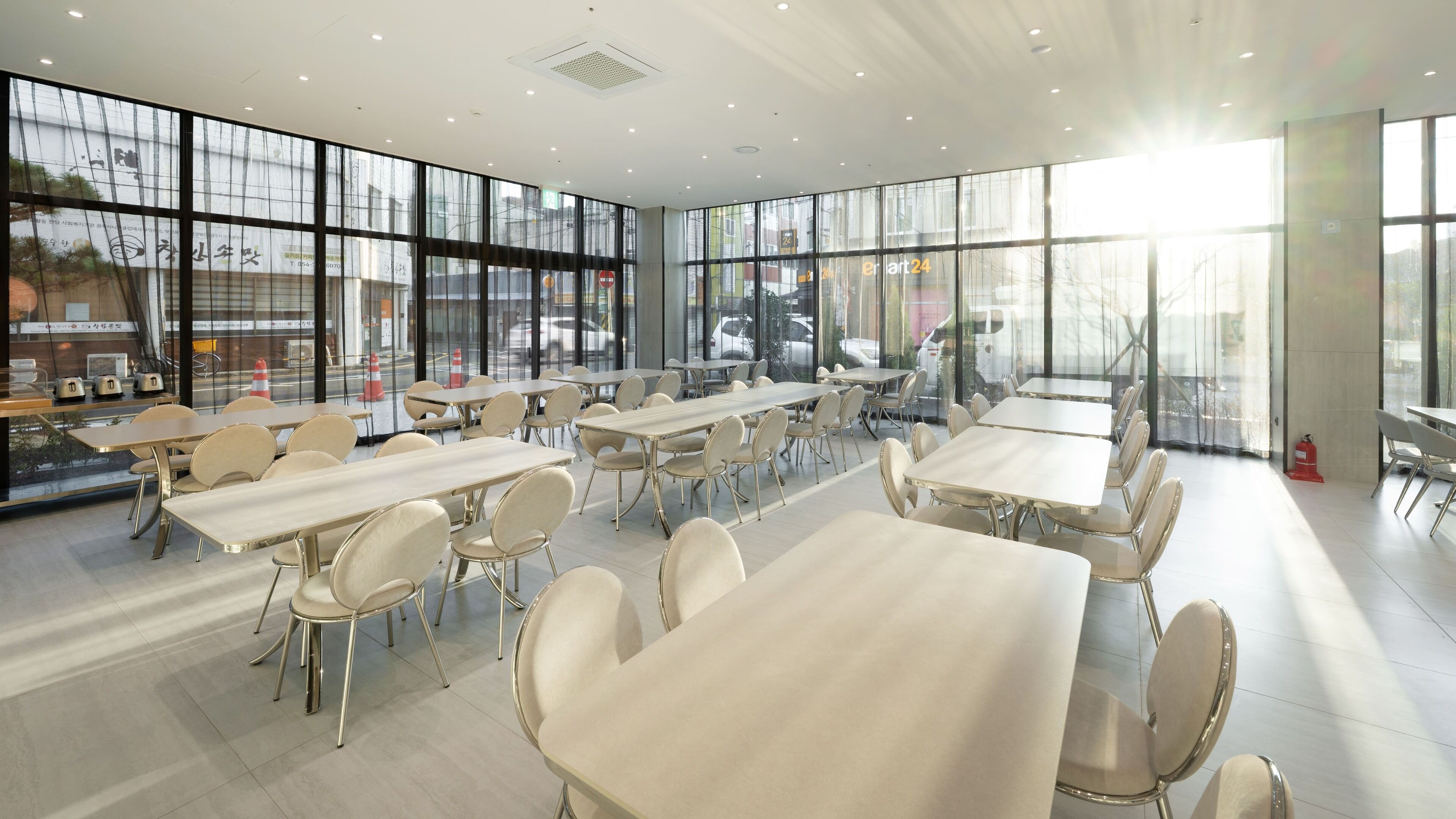 Un amplio comedor interior con varias mesas y sillas, ventanas grandes y un diseño moderno y limpio.