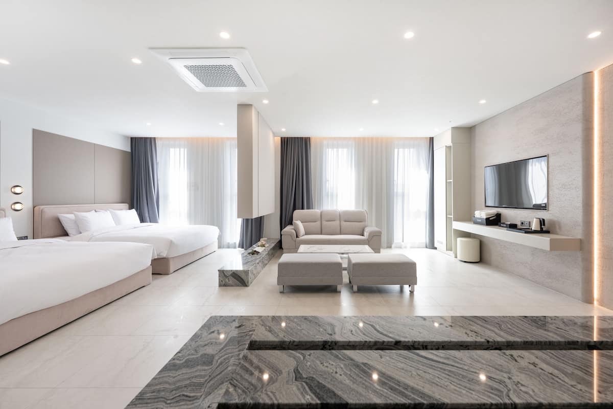 Quarto de hotel moderno com uma cama grande, um sofá, uma televisão e piso de mármore.