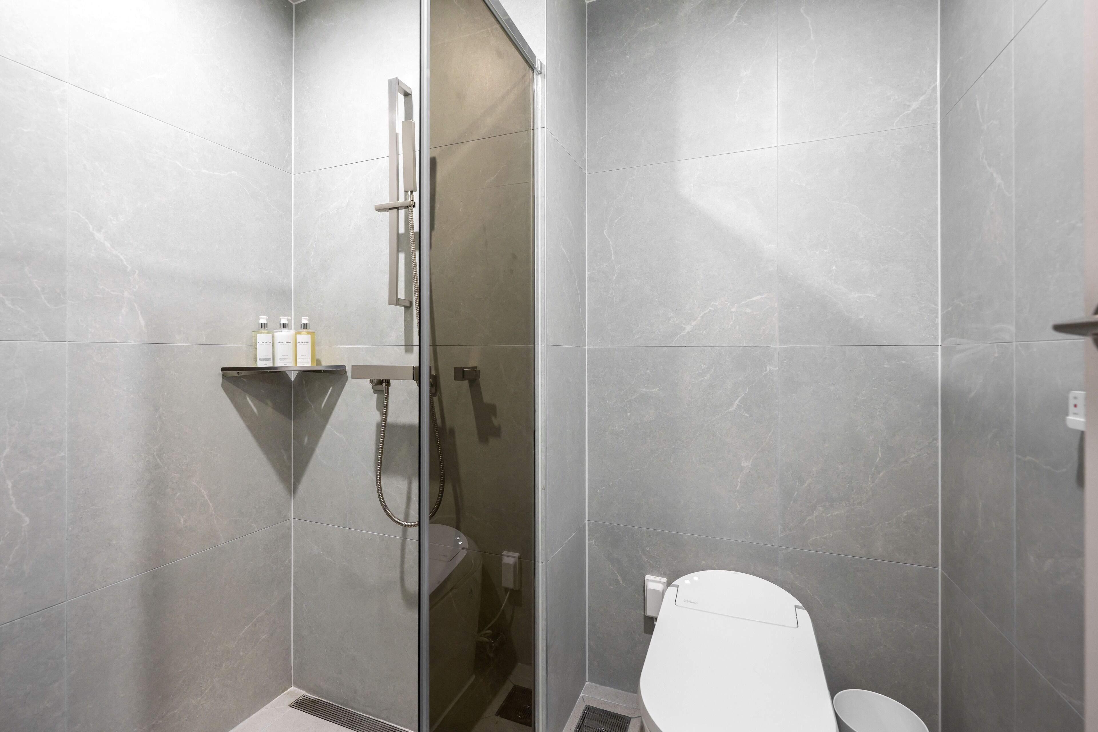 Ein modernes Badezimmer mit einer gläsernen Duschkabine, einer weißen Toilette und einem Ablagebereich für Toilettenartikel.