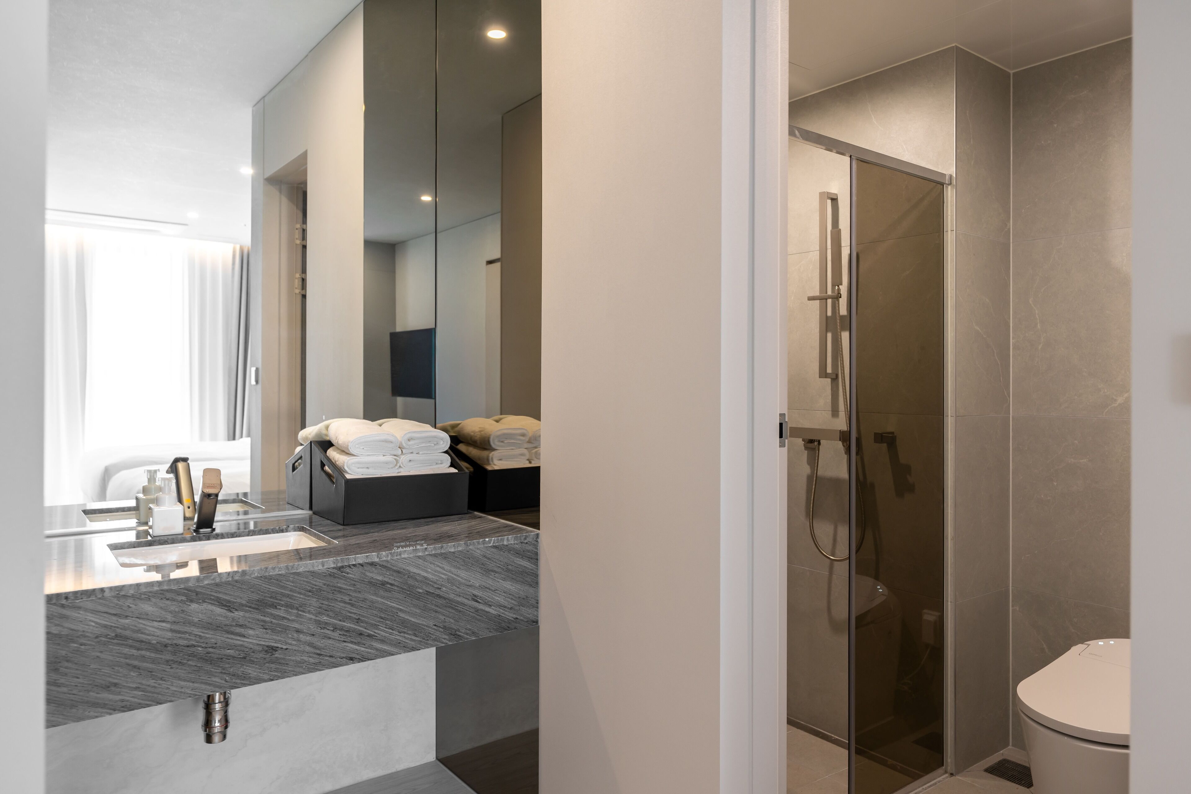A modern bathroom with a glass-enclosed shower, a marble sink, and neatly folded towels.