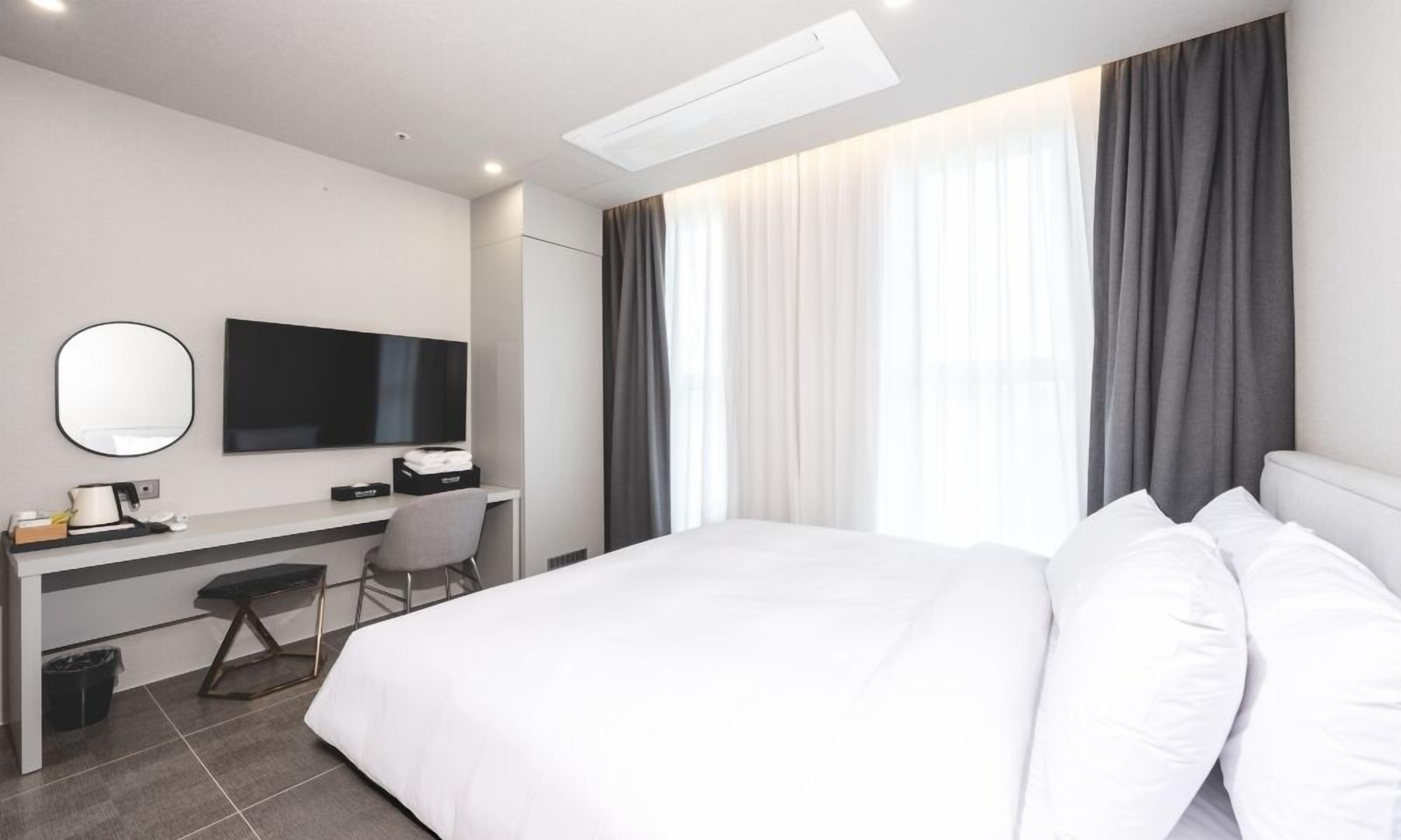 A hotel room with a bed, a desk, a chair, a television, and a window with curtains.