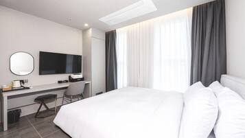 A hotel room with a bed, a desk, a chair, a television, and a window with curtains.