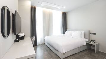 A modern hotel room with a large bed, a bedside table with a phone, a desk with a mirror, and a chair.