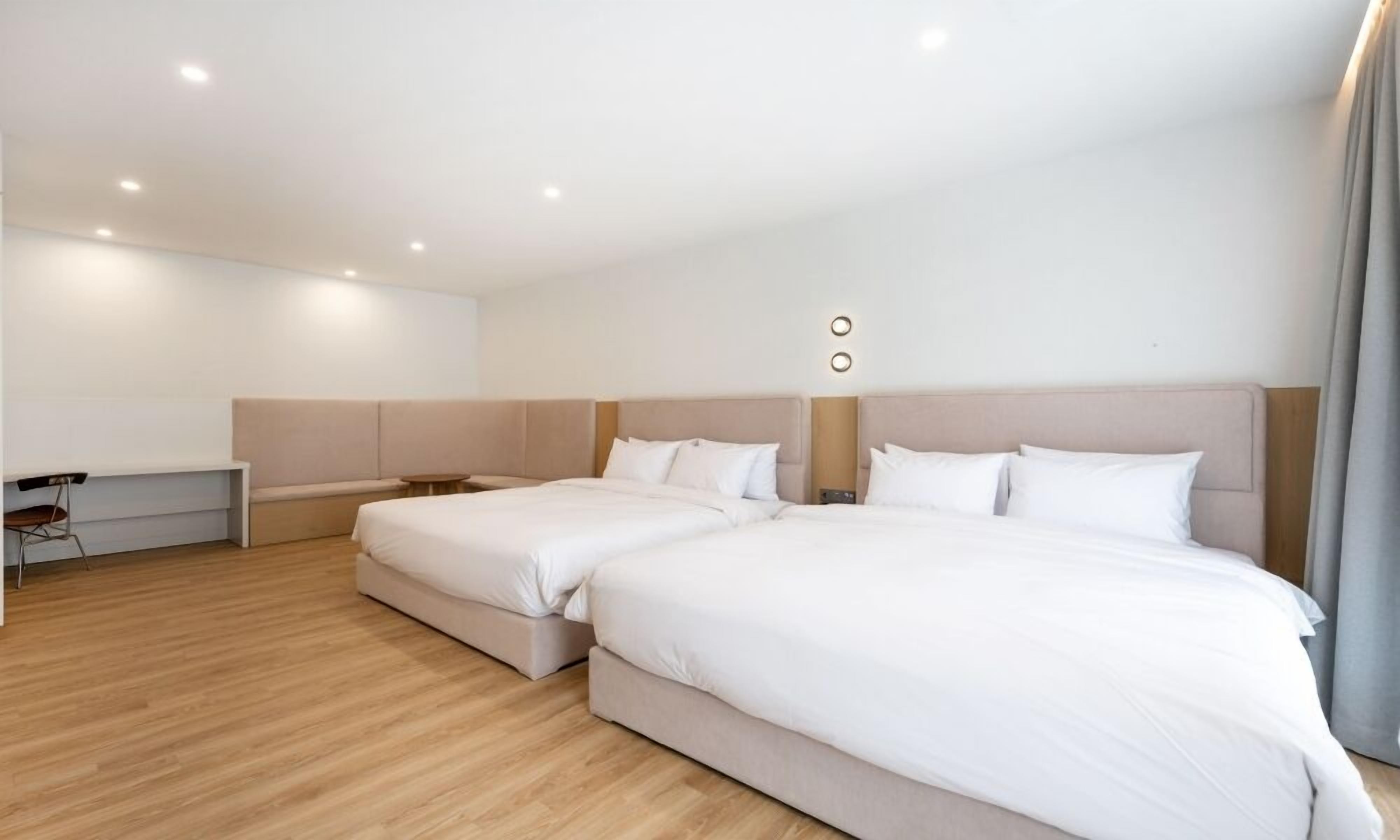 A modern hotel room with two beds, a desk, and a chair.