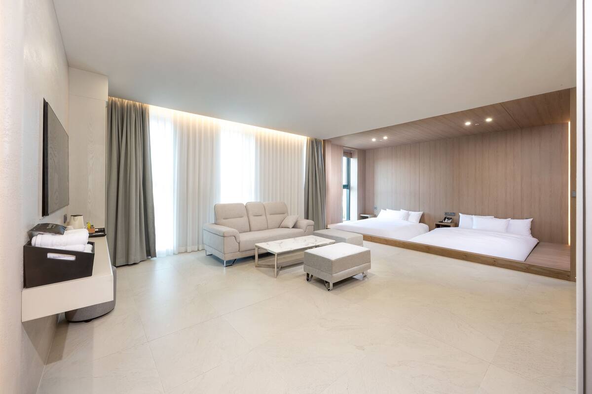 Quarto de hotel moderno com sofá, cama, mesa de centro e televisão em suporte.