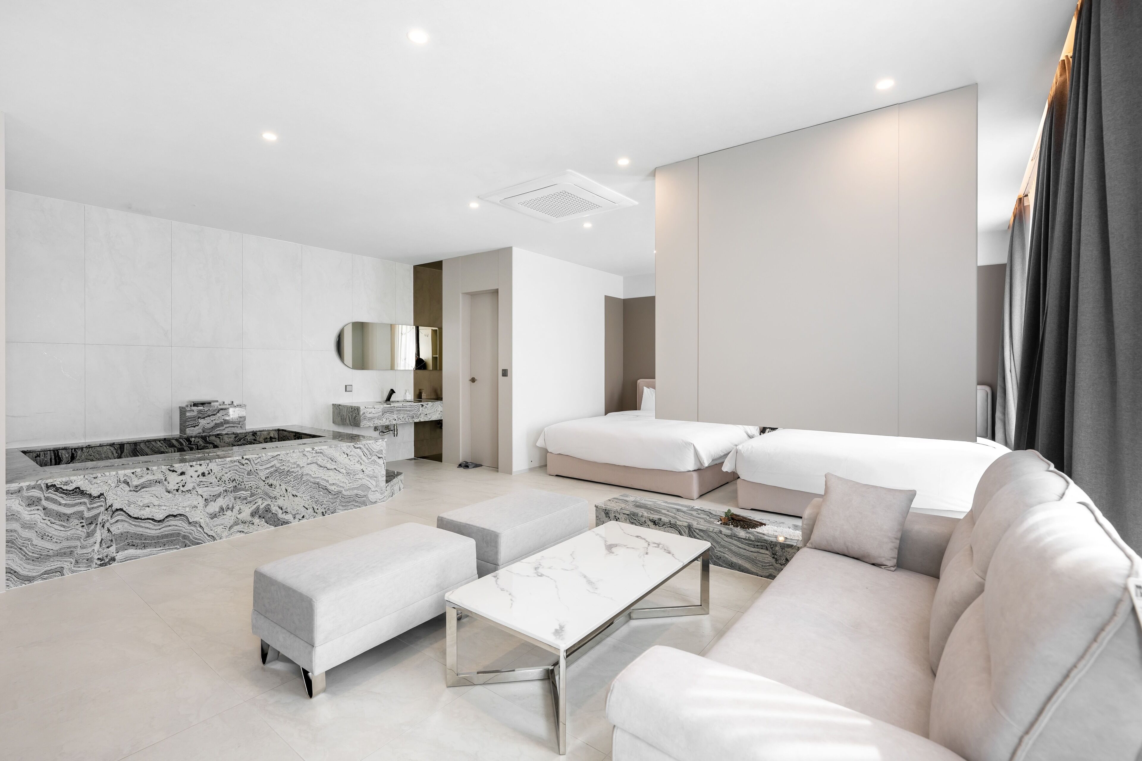 Une chambre d’hôtel moderne avec une salle de bain en marbre, un canapé, un lit et une petite table.