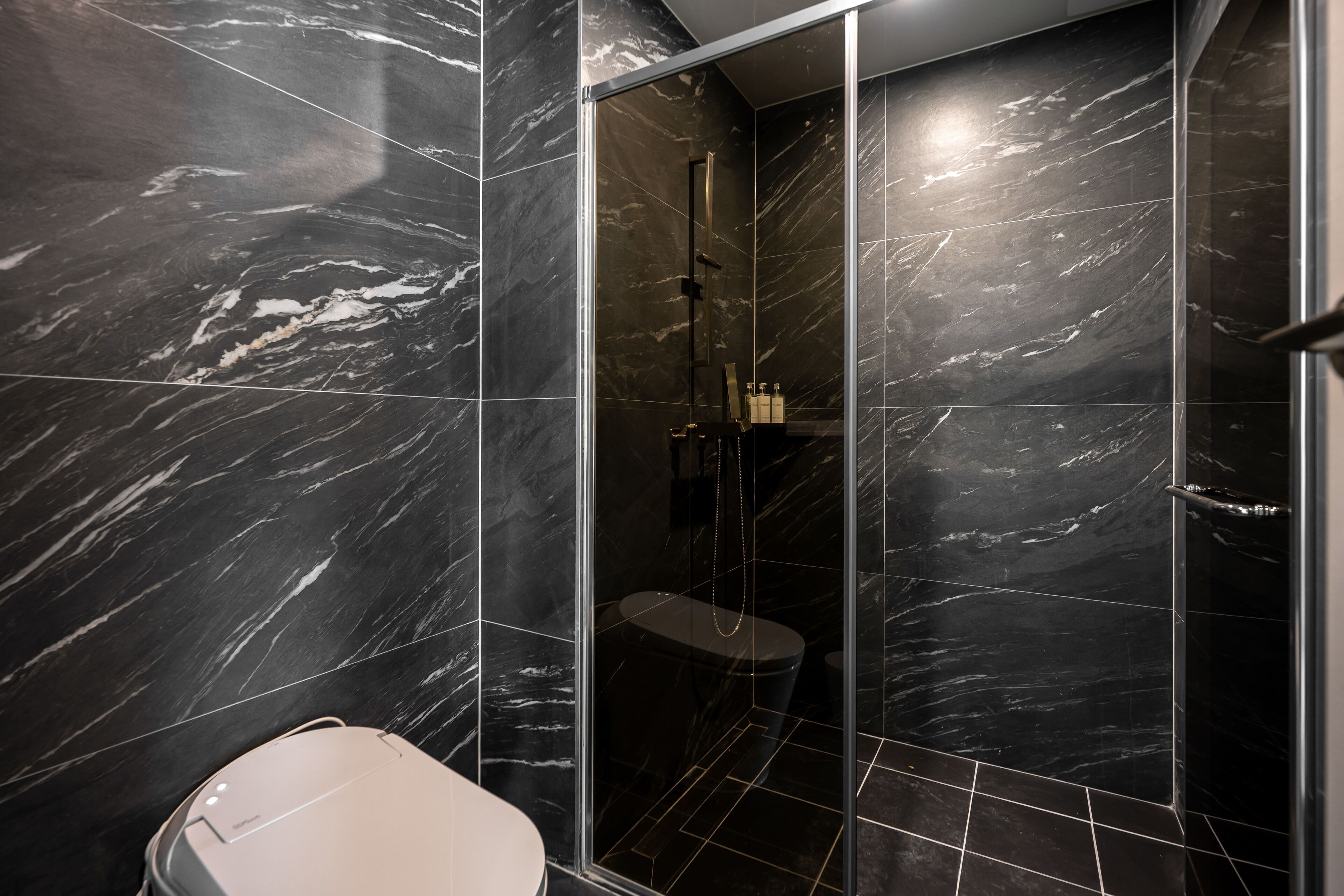 Un baño moderno con baldosas de mármol negro, ducha con cerramiento de vidrio y un inodoro.