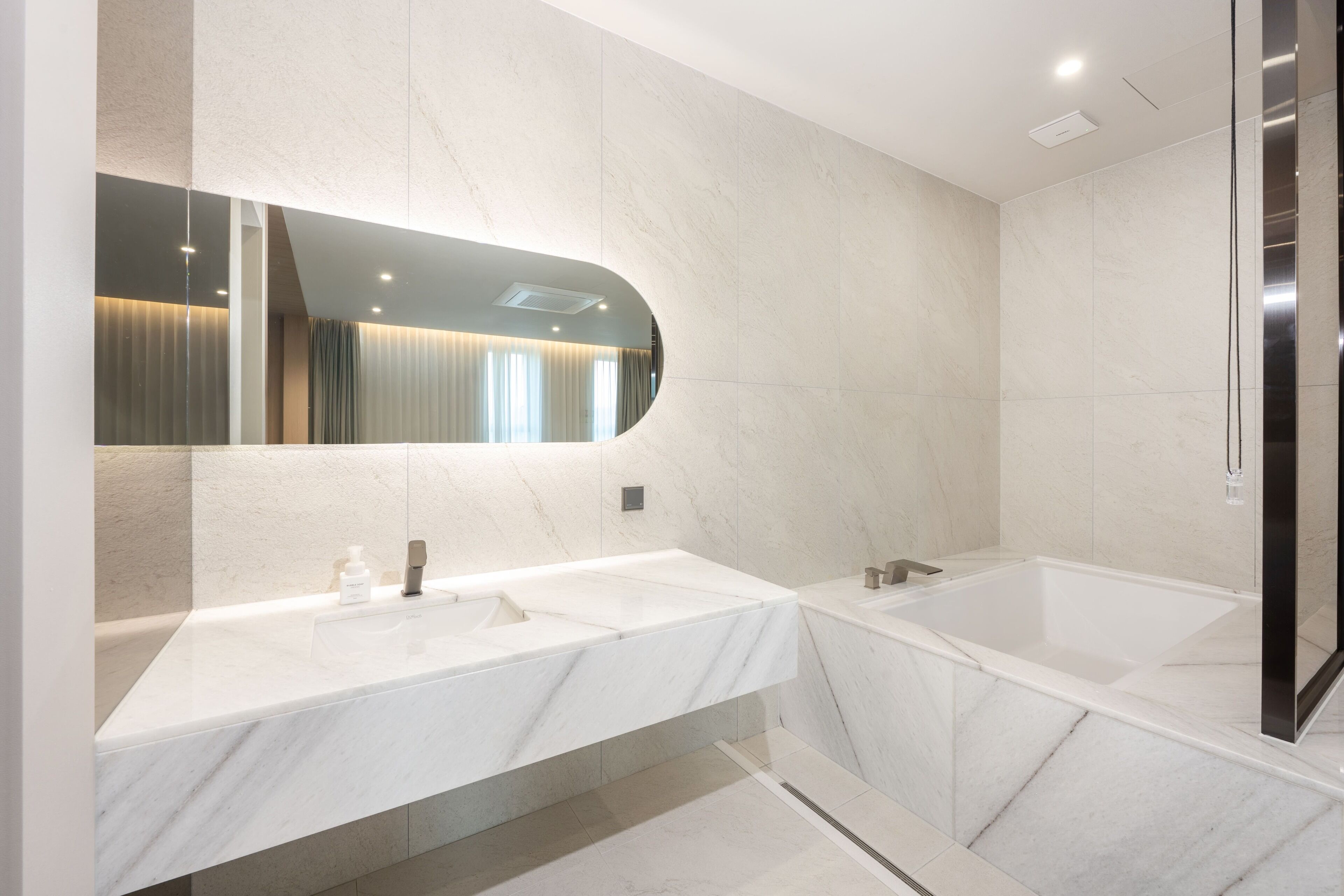 A modern bathroom with two sinks, a large mirror, and a bathtub.