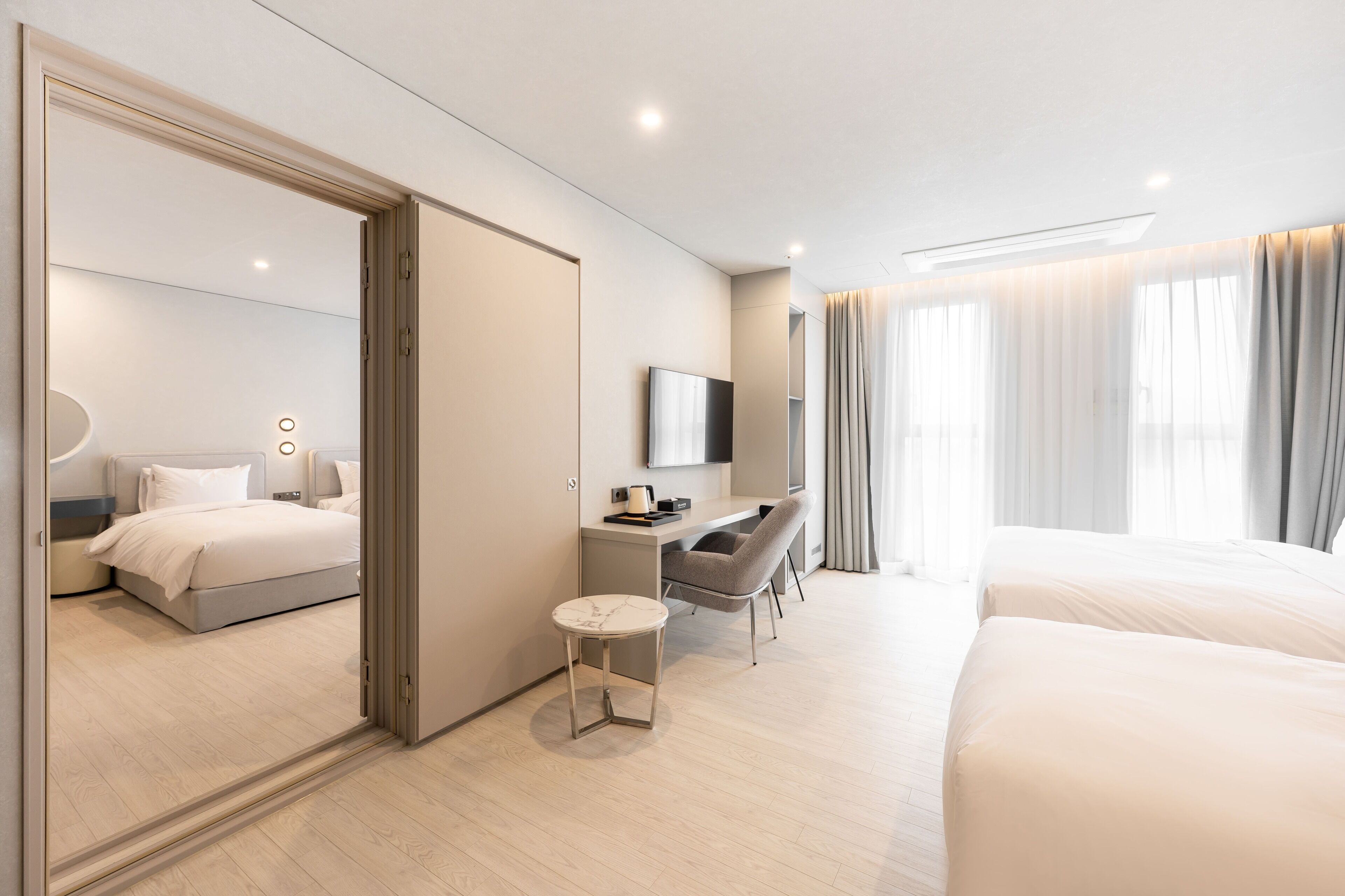 A modern hotel room with a bed, desk, chair, and a small round table.