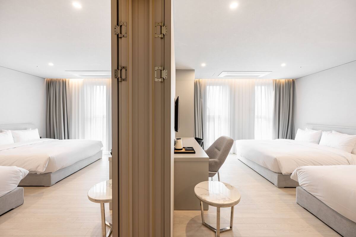 Quarto de hotel com duas camas, uma mesa de trabalho com cadeira e uma televisão.