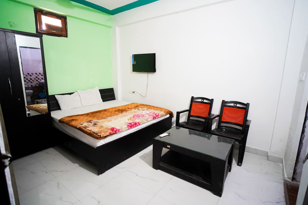 A bedroom with a bed, a TV mounted on the wall, a desk, and two chairs.