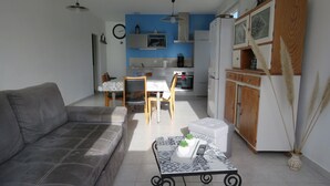 Un salon avec un canapé gris, une table à manger avec des chaises, un coin cuisine équipé d’un réfrigérateur, d’un four à micro-ondes et de placards.
