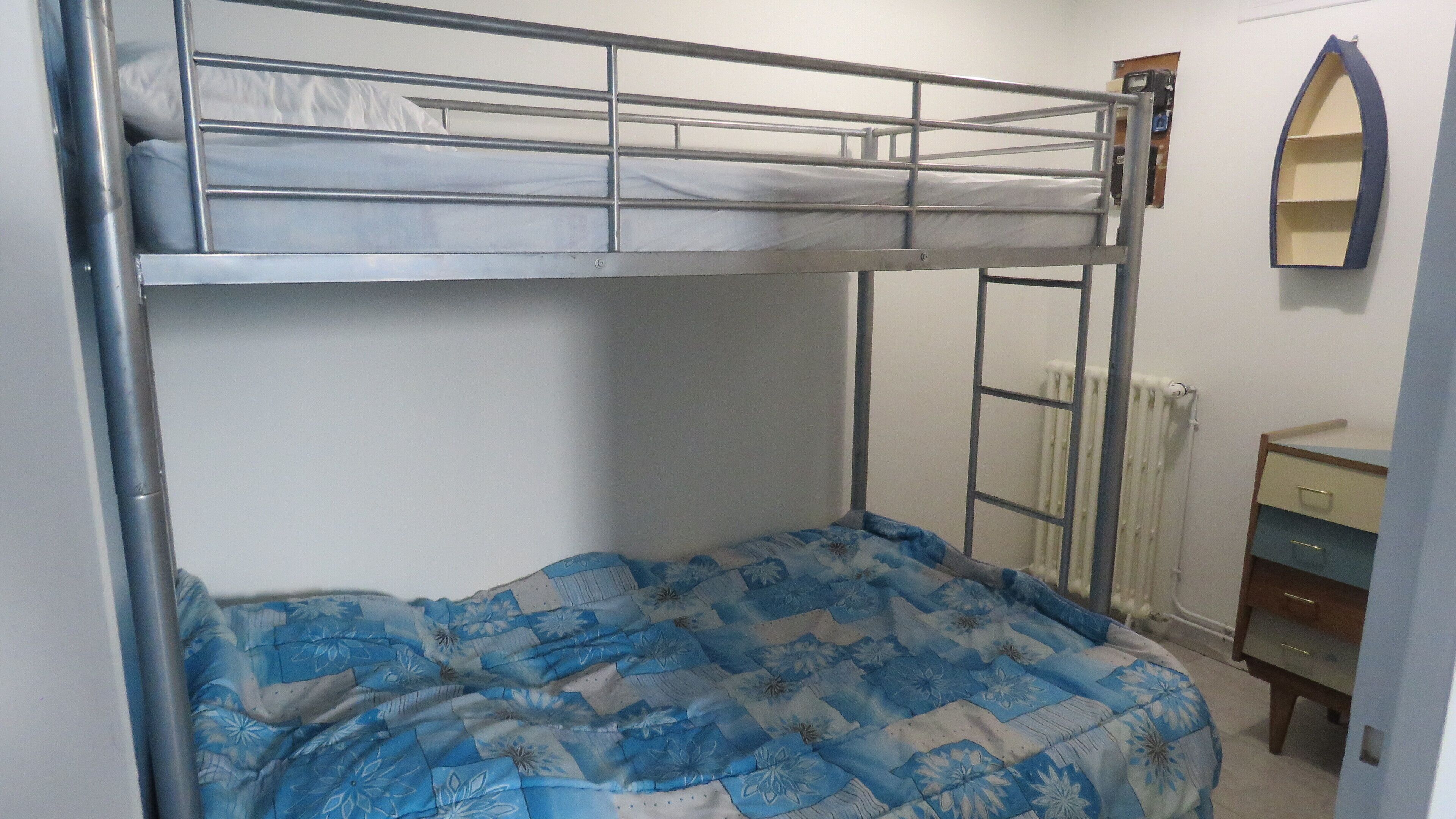 A bunk bed with a lower bunk and a mattress with a floral pattern. There is a dresser with drawers and a mirror on the wall.