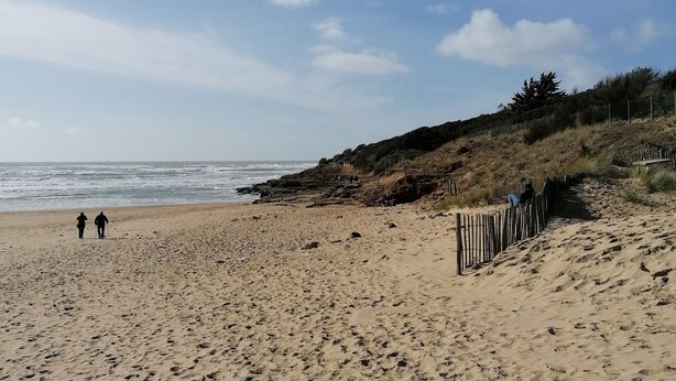 Une plage de sable avec des empreintes, une clôture en bois et un ciel dégagé.