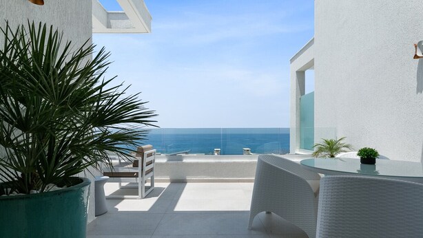 A balcony with a view of the sea, white walls, and potted plants.