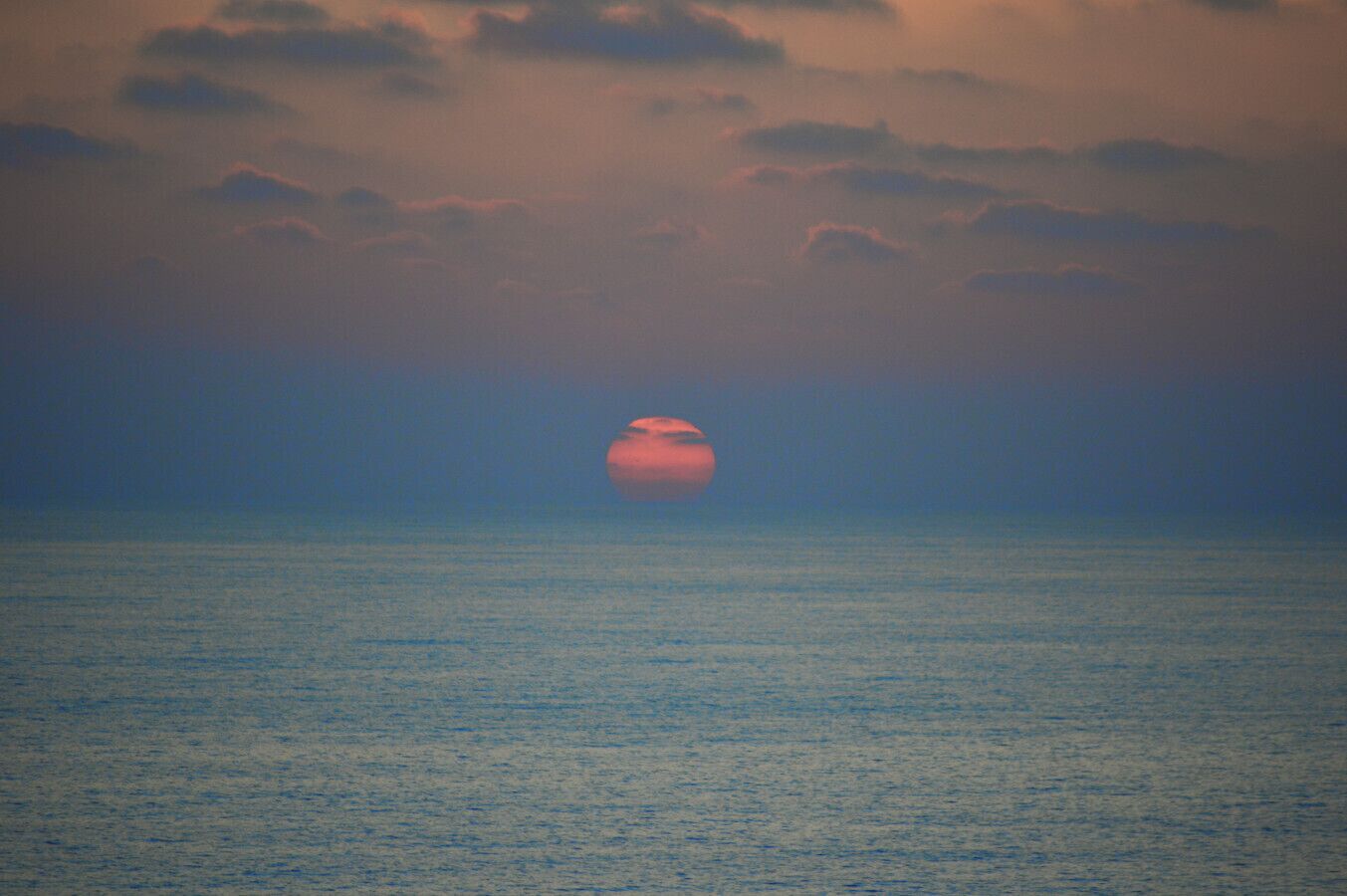 Een zonsondergang boven een rustige zee met een heldere lucht.
