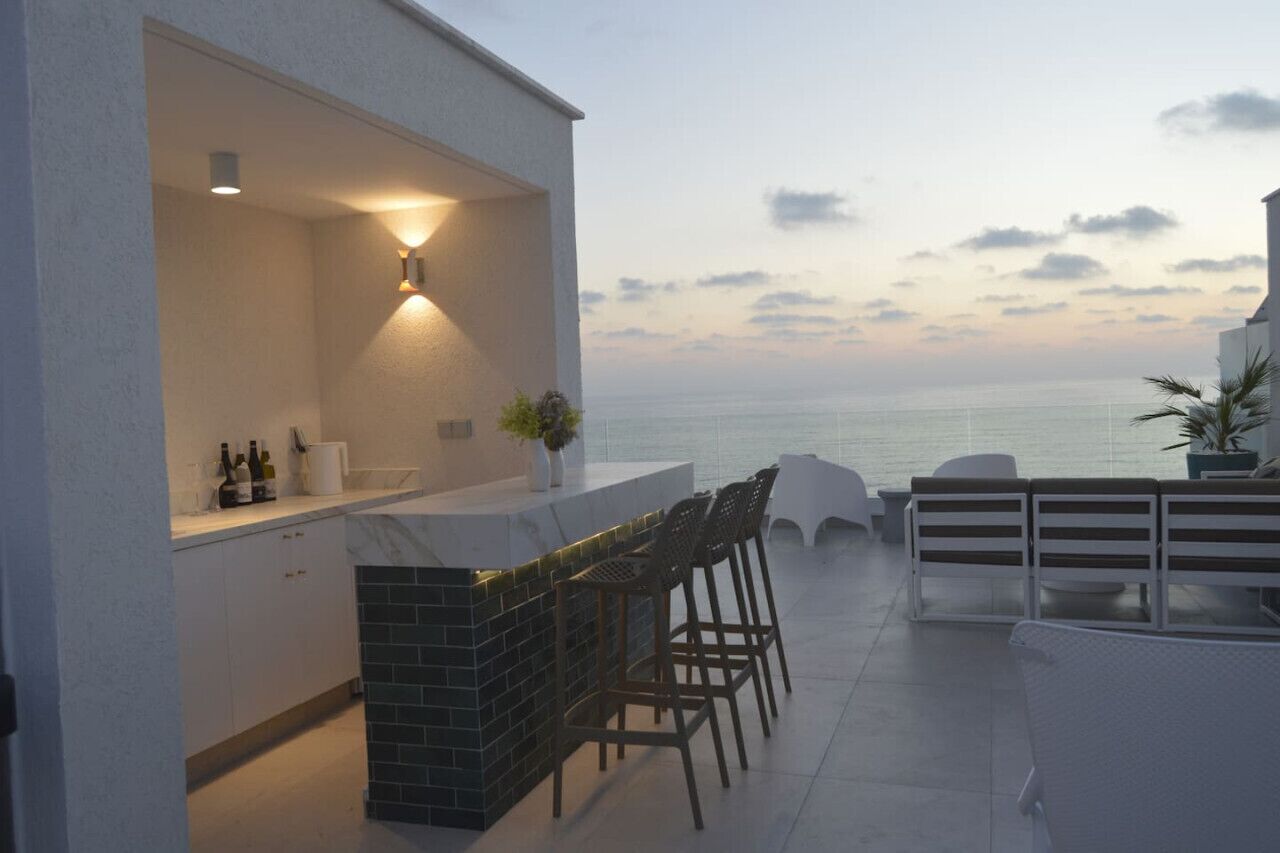 An outdoor bar area with a view of the sea, a white exterior wall, and a tiled floor.