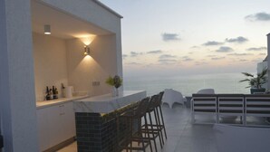 An outdoor bar area with a view of the sea, a white exterior wall, and a tiled floor.