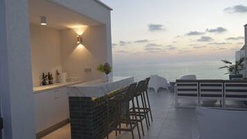 An outdoor bar area with a view of the sea, a white exterior wall, and a tiled floor.