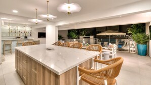 A modern kitchen with a marble island, wicker chairs, and pendant lighting.
