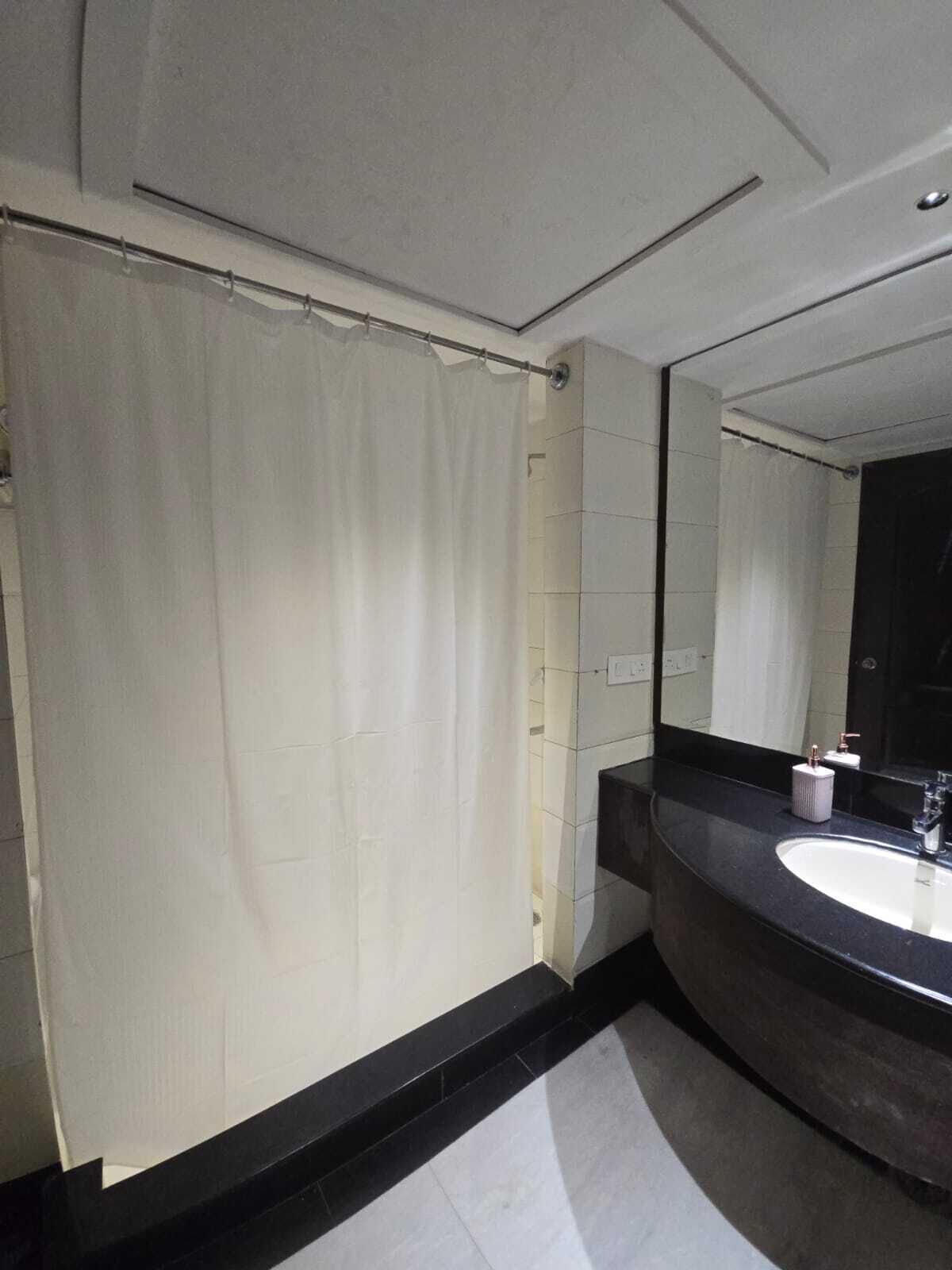 A bathroom with a white shower curtain, a black countertop, and a mirror.