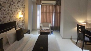 A hotel room with a large bed, a desk, a chair, an air conditioning unit, and a patterned wall. - Hotel Supreme Suites Ludhiana  (Ludhiana)