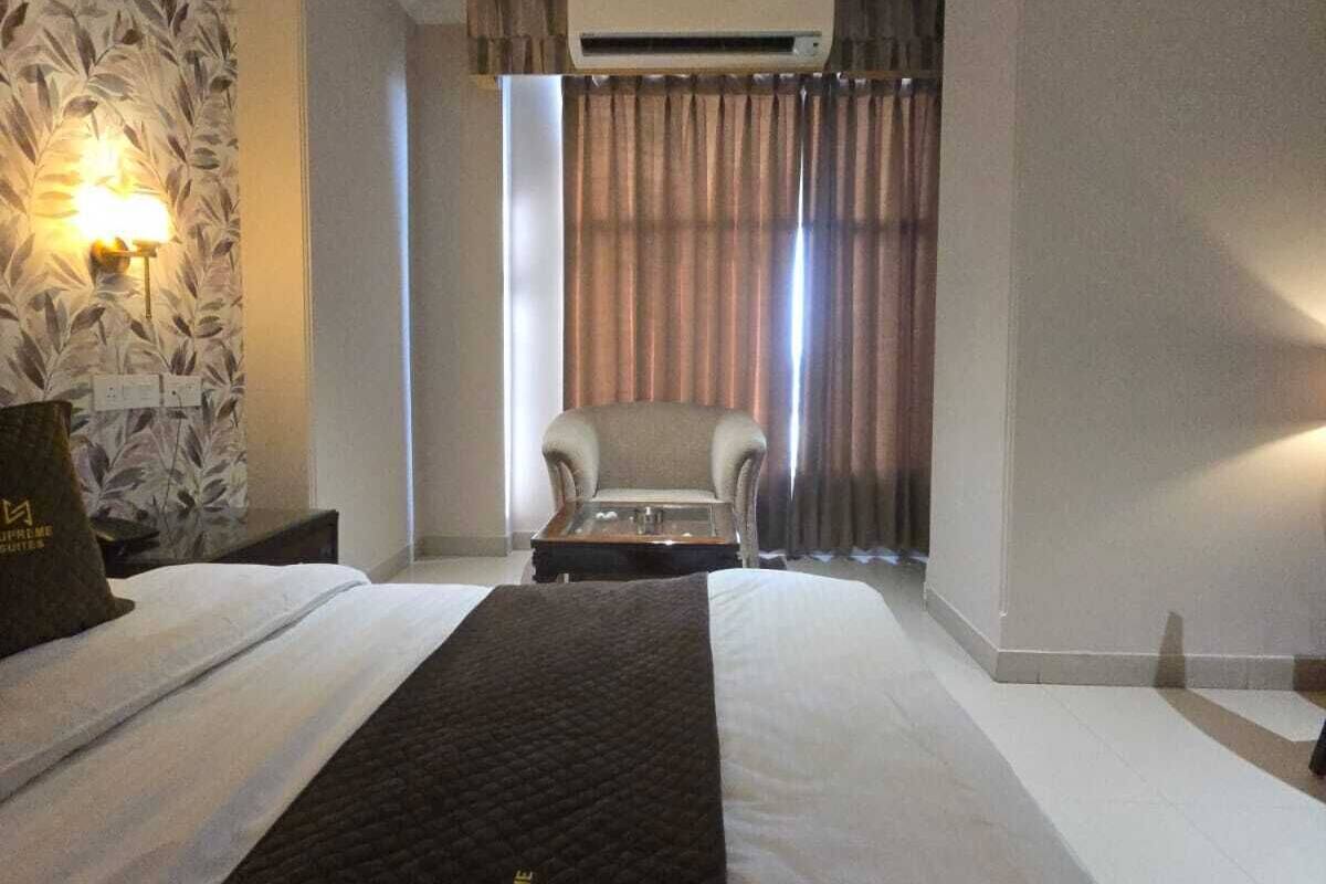 Habitación de hotel con una cama grande, una silla, una mesita pequeña y un aire acondicionado en la pared.