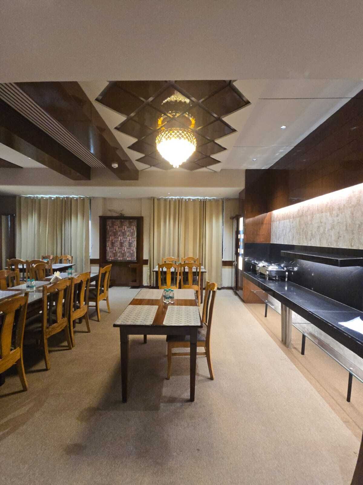 Un comedor con mesas y sillas de madera, una lámpara central y una barra larga con estufa.