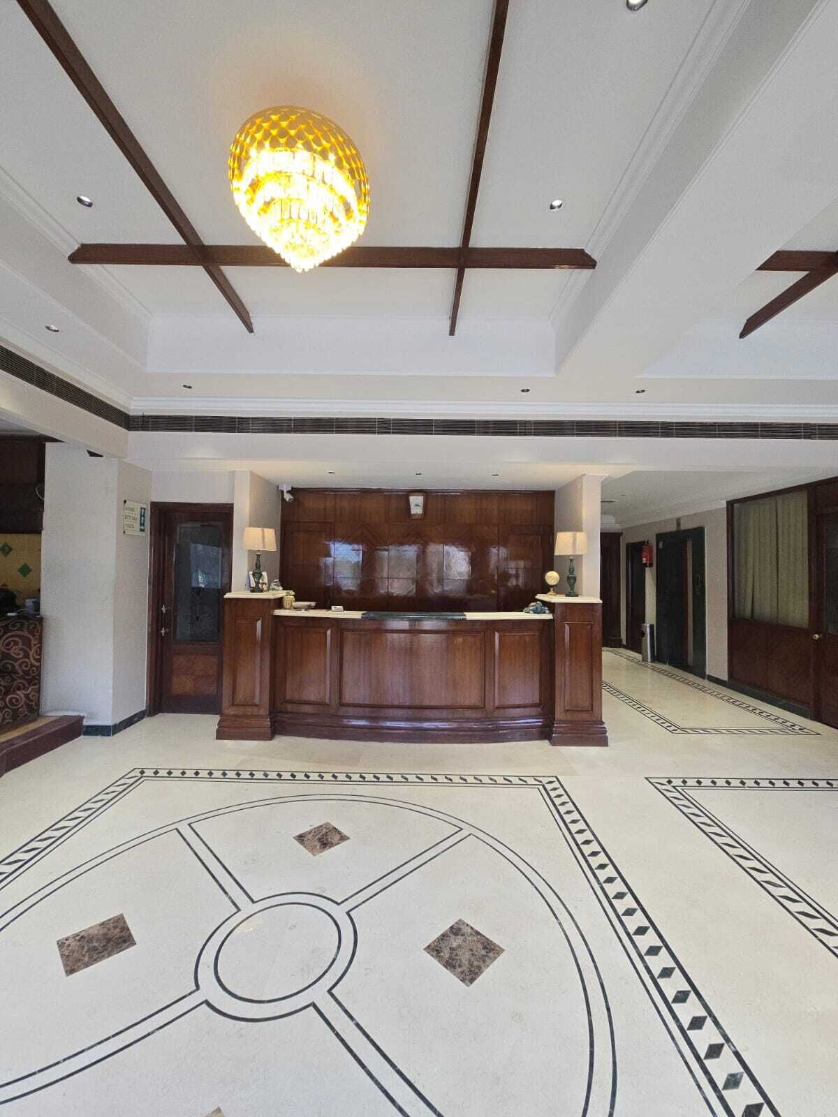 A lobby with a large wooden reception desk, a patterned floor, and a chandelier.