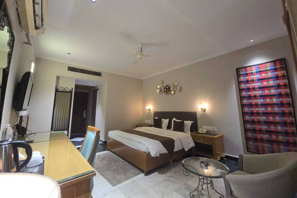 Habitación de hotel con cama, mesita de noche, silla, escritorio y televisor.