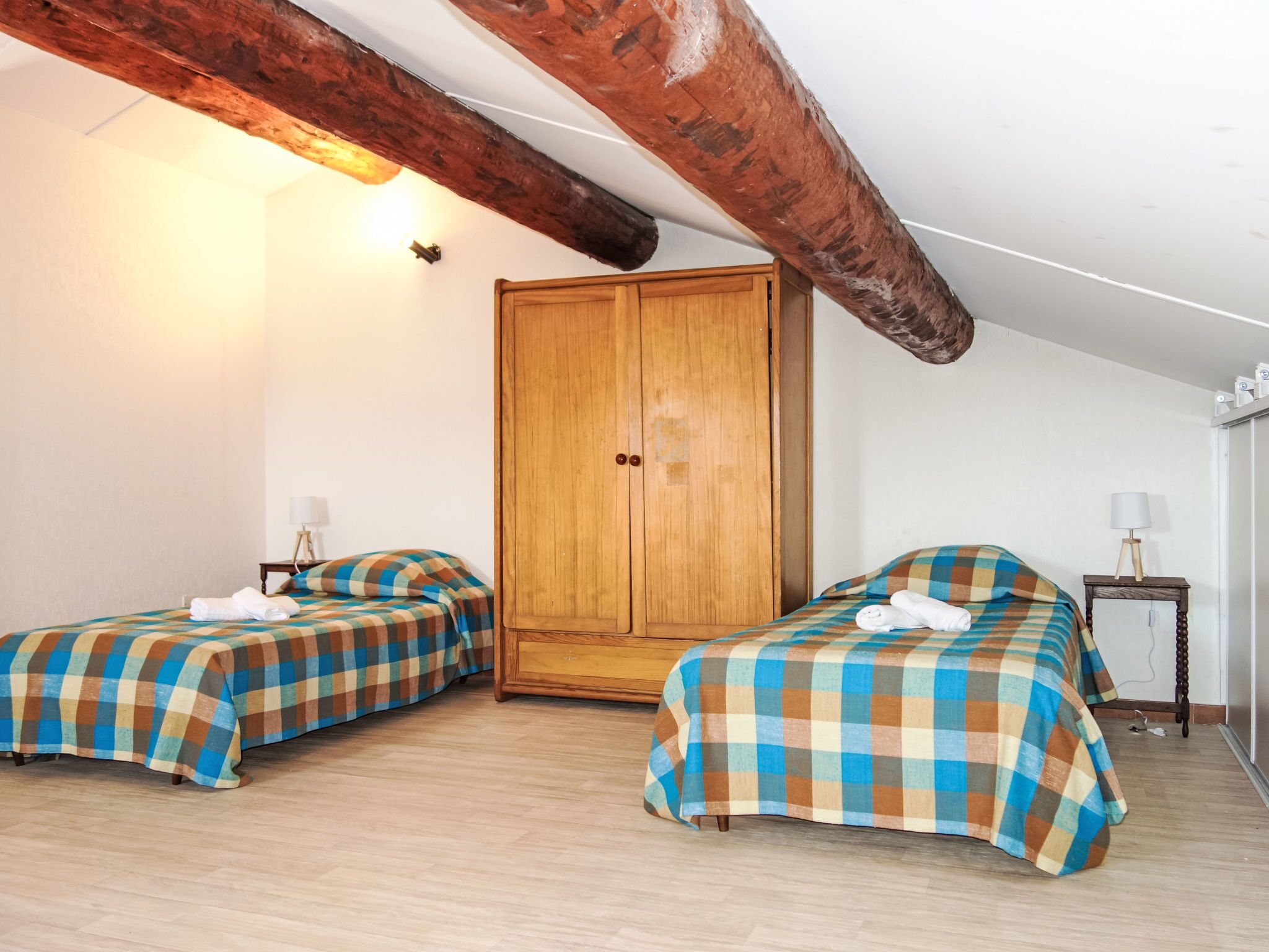 Une chambre avec deux lits, une armoire en bois et une poutre en bois au plafond.