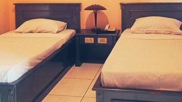 A hotel room with two single beds, each with a pillow and a nightstand with a lamp.