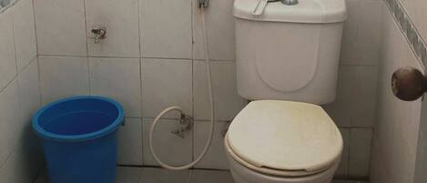 Um banheiro pequeno com vaso sanitário, um balde azul e suporte para papel higiênico.