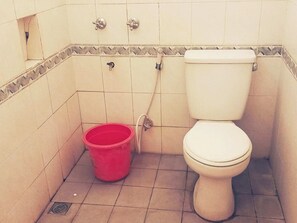 A small bathroom with a toilet, a red bucket, and a shower drain.