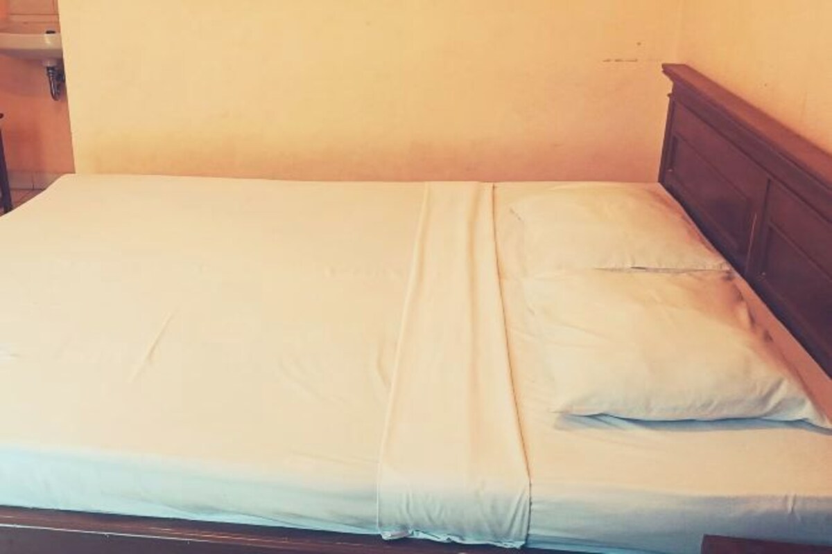 Una cama individual con cabecera de madera en una habitación con paredes lisas.