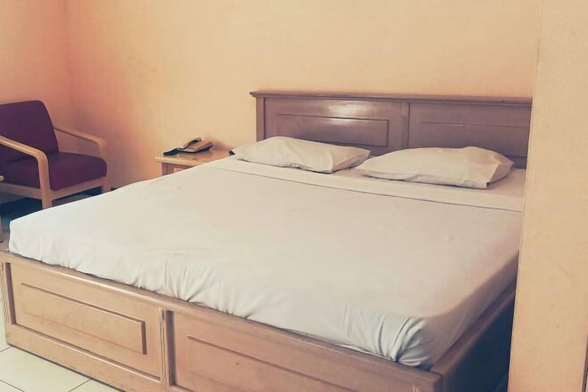 A single bed with a wooden headboard, a nightstand with a lamp, and a chair.
