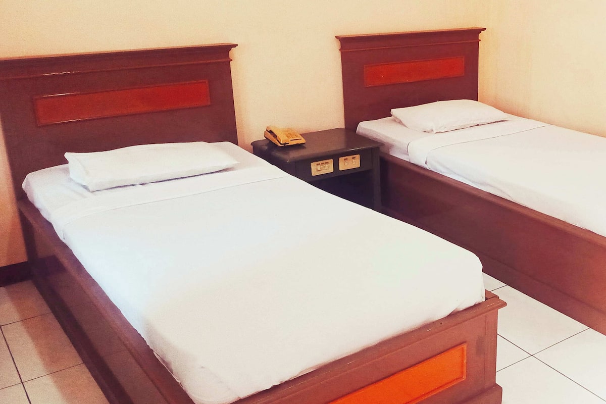Two single beds with wooden headboards, white linens, and a small bedside table with a telephone.