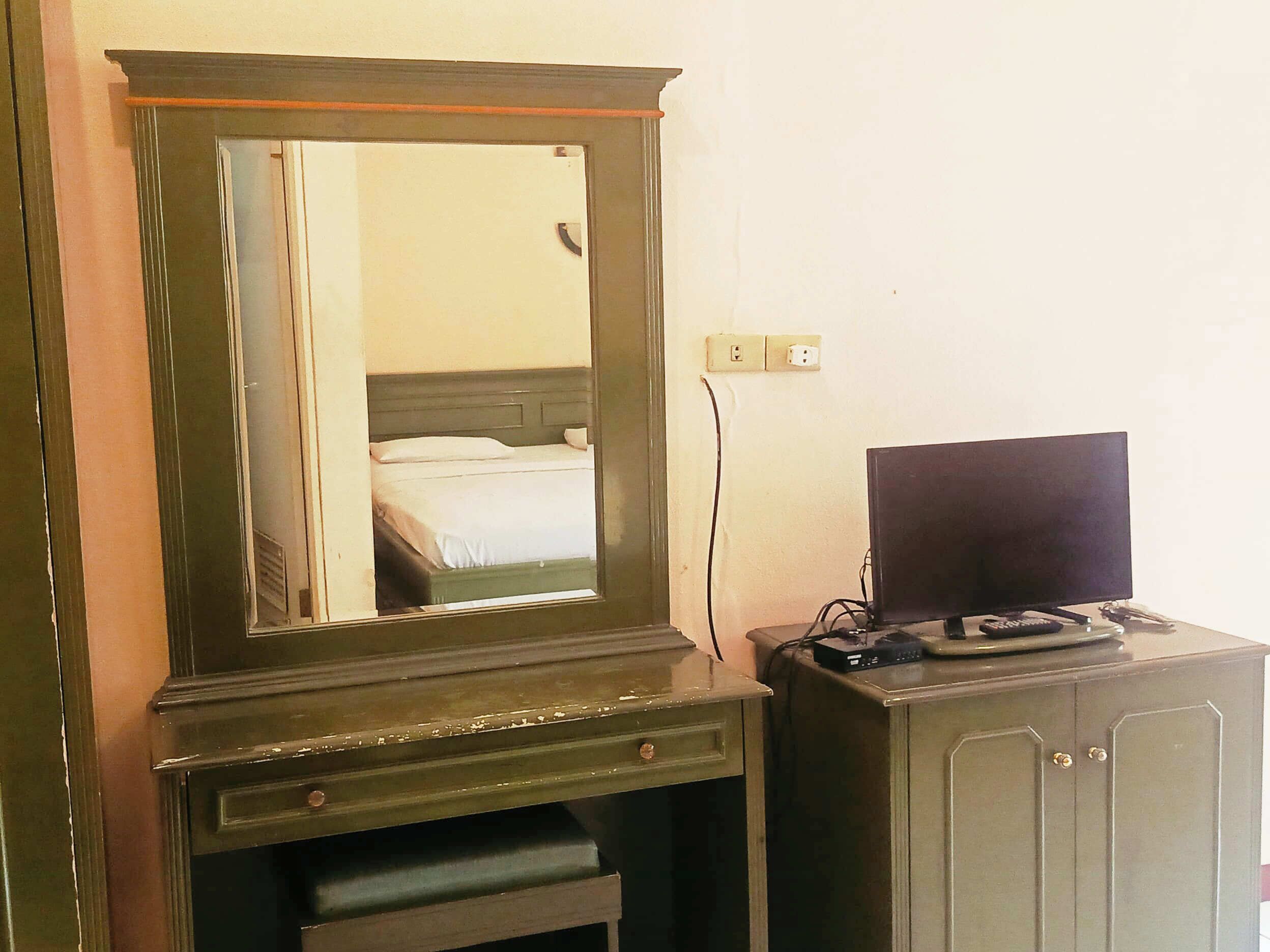 Ein Zimmer mit einem großen Spiegel, einem Bett, einem Fernseher auf einer Kommode und einer Steckdose an der Wand.