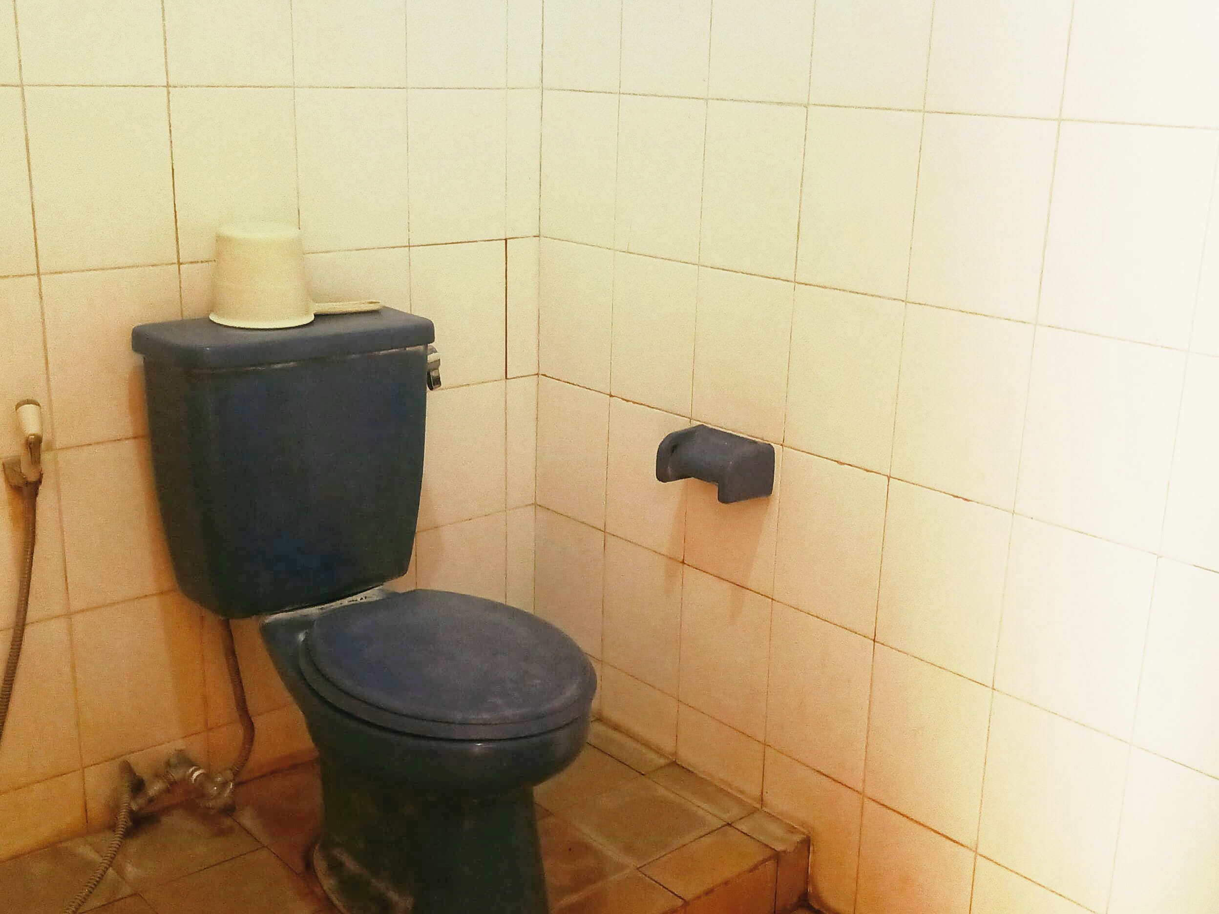 Een eenvoudige badkamer met toilet, toiletrolhouder en een zichtbare leiding op de vloer.