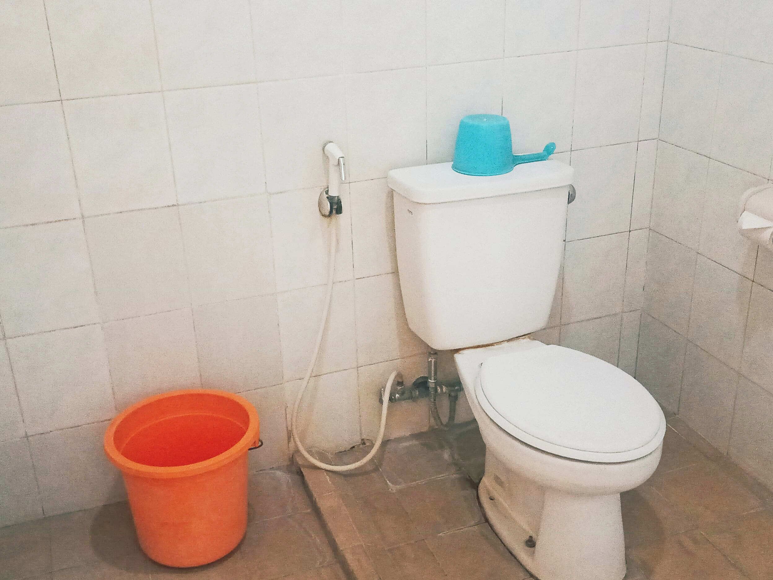 Un baño con inodoro, manguera de ducha y un balde.