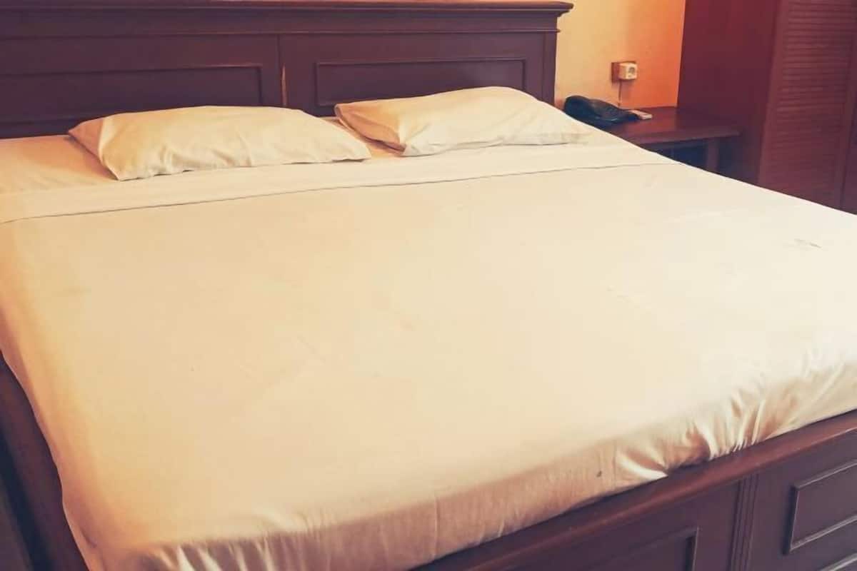 A neatly made bed with a wooden headboard, a bedside table with a phone, and a wall socket.