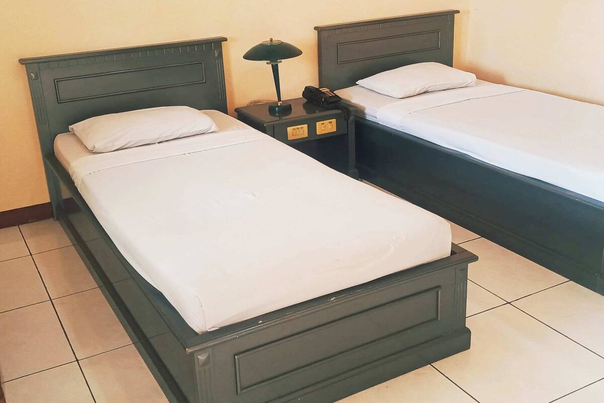 Two twin beds with wooden headboards, a nightstand with a lamp, and a phone.