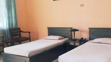 A hotel room with two single beds, a nightstand with a lamp, a chair, and a painting on the wall.