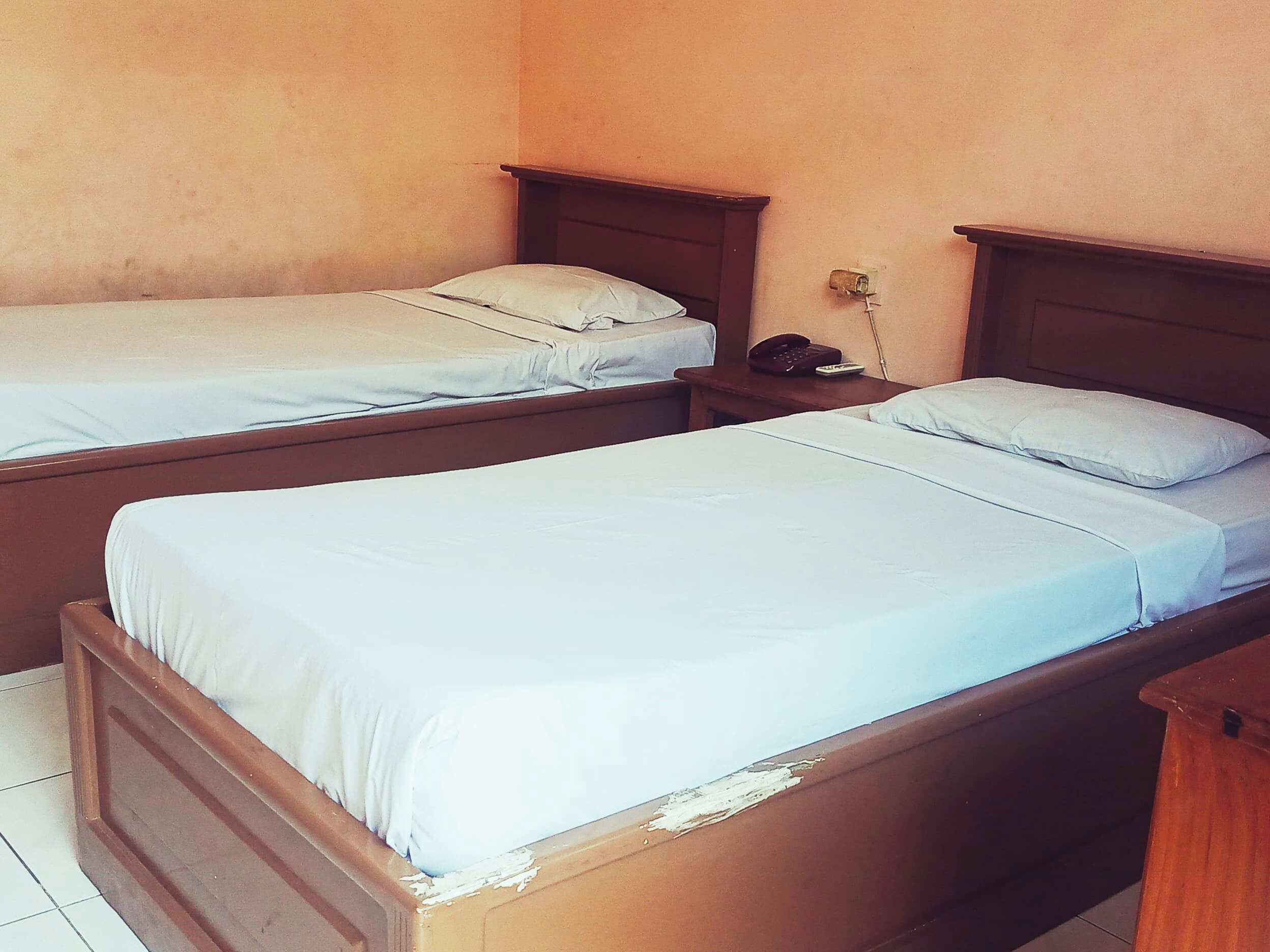 A room with two single beds, wooden headboards, a bedside table with a phone, and a wall socket.