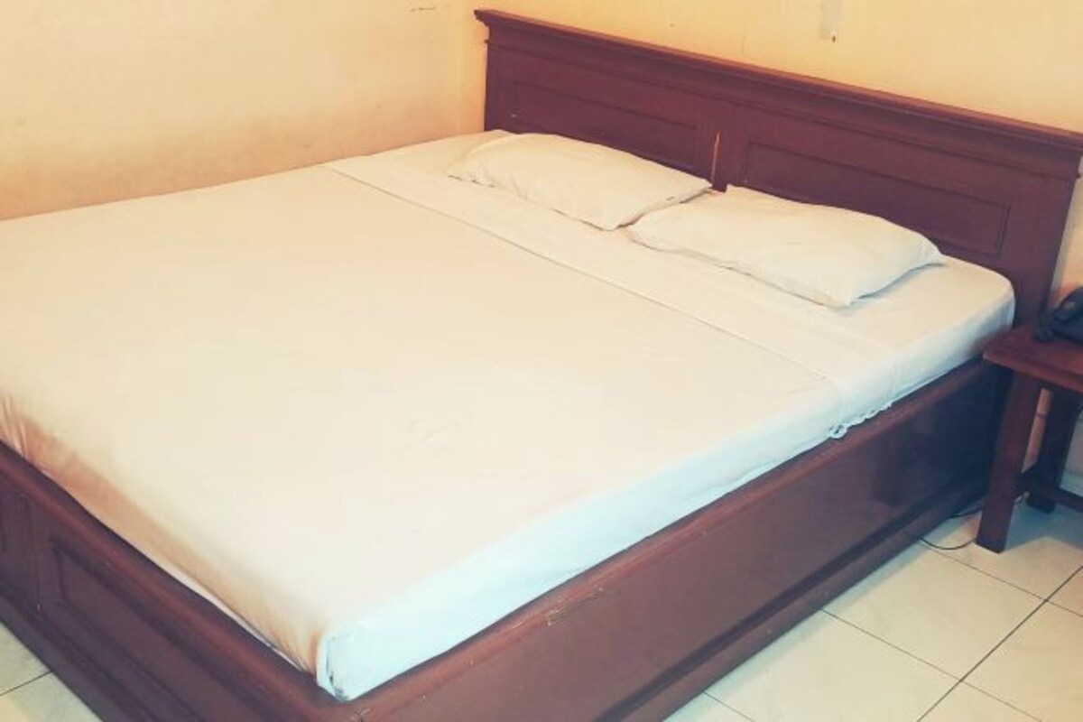 Una cama individual con cabecera de madera, ropa de cama blanca y una mesita de noche con lámpara.