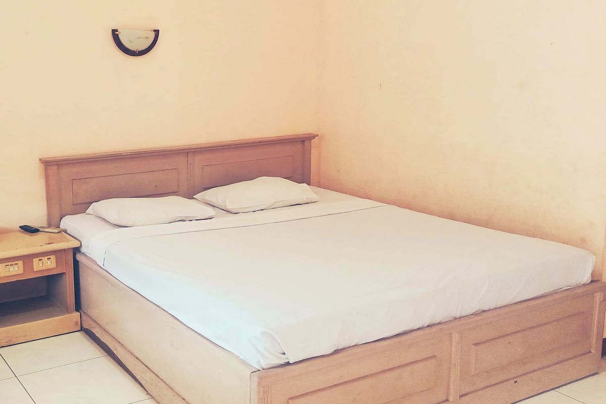 A single bed with a wooden headboard and white bedding in a room with plain walls and a small bedside table.